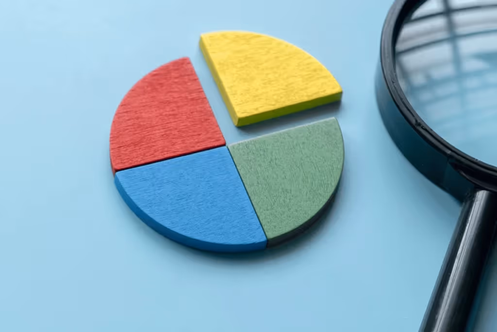 Colorful wooden pie chart segments on a light blue background with a magnifying glass.