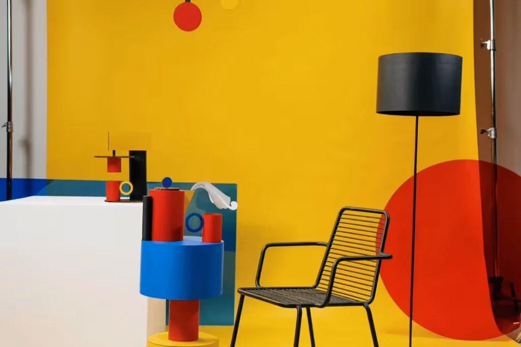 Modern room with yellow walls, colorful abstract decor, black chair, and a floor lamp.