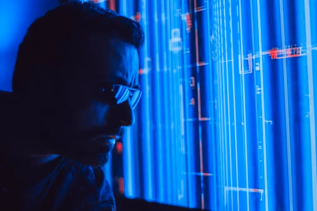 Silhouetted figure in front of a screen with blue digital data visualization.