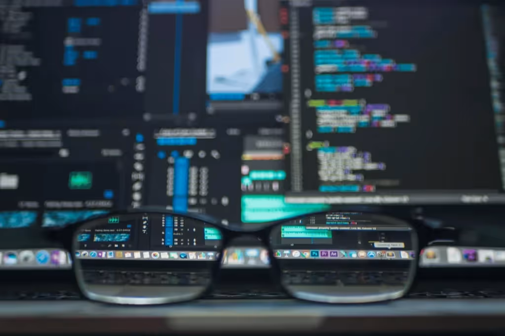 Close-up of computer code reflected in glasses, showcasing a programming environment on a laptop screen.