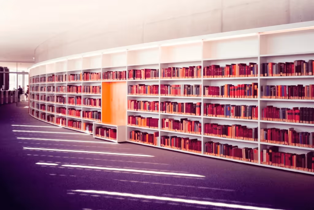 Curved white bookshelves filled with red books in a library with purple carpet.