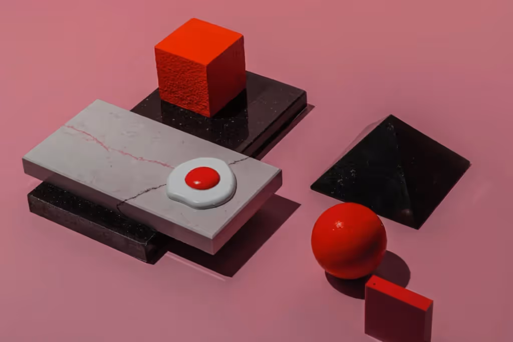 A collection of colorful geometric shapes, including red spheres, cubes, and pyramids, set against a pink background.