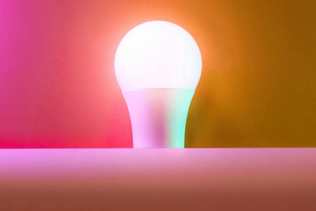 White LED light bulb on a pink shelf against a vibrant orange and pink gradient background.