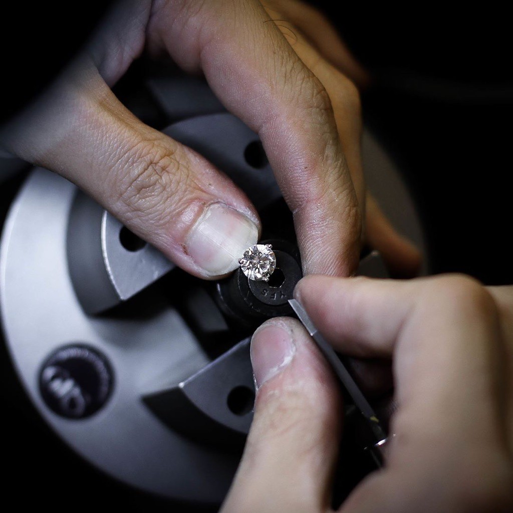 Close-up of hands holding a diamond on a jeweler's tool for precise cutting or polishing.