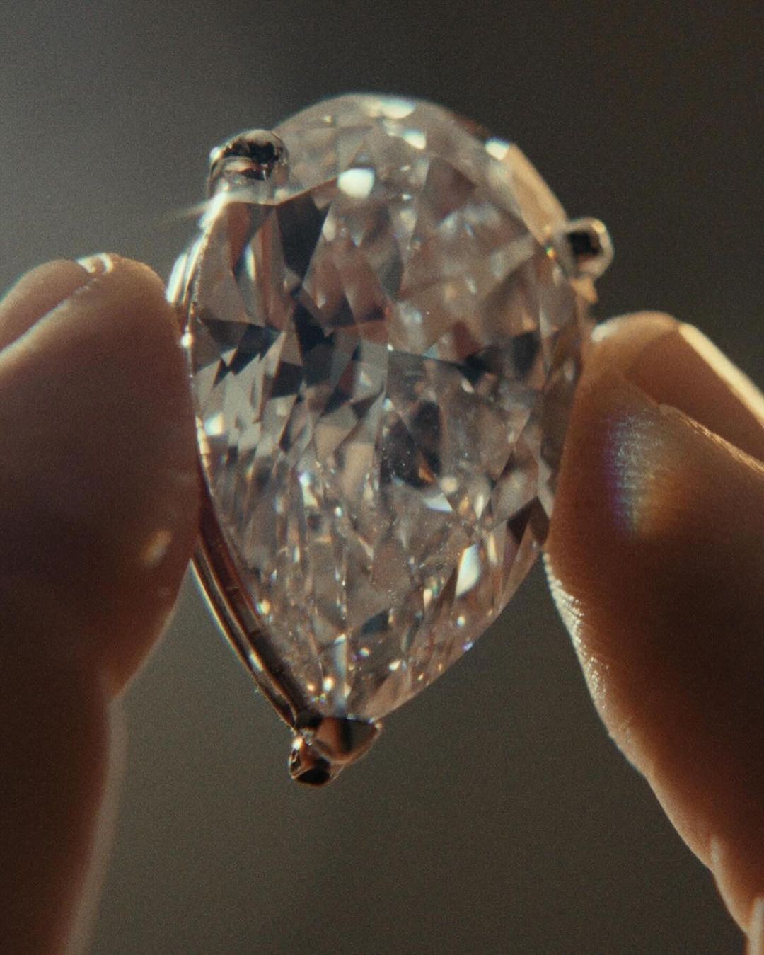 Close-up of hands holding a pear-shaped faceted diamond with metal prongs.