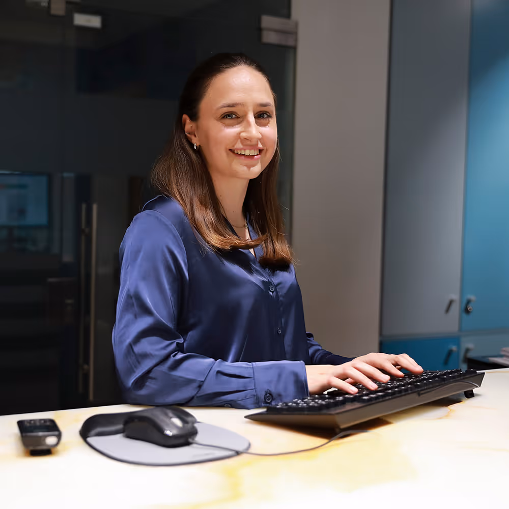 A staff member at Theranosticum is typing on a keyboard at a bright desk with a computer mouse.