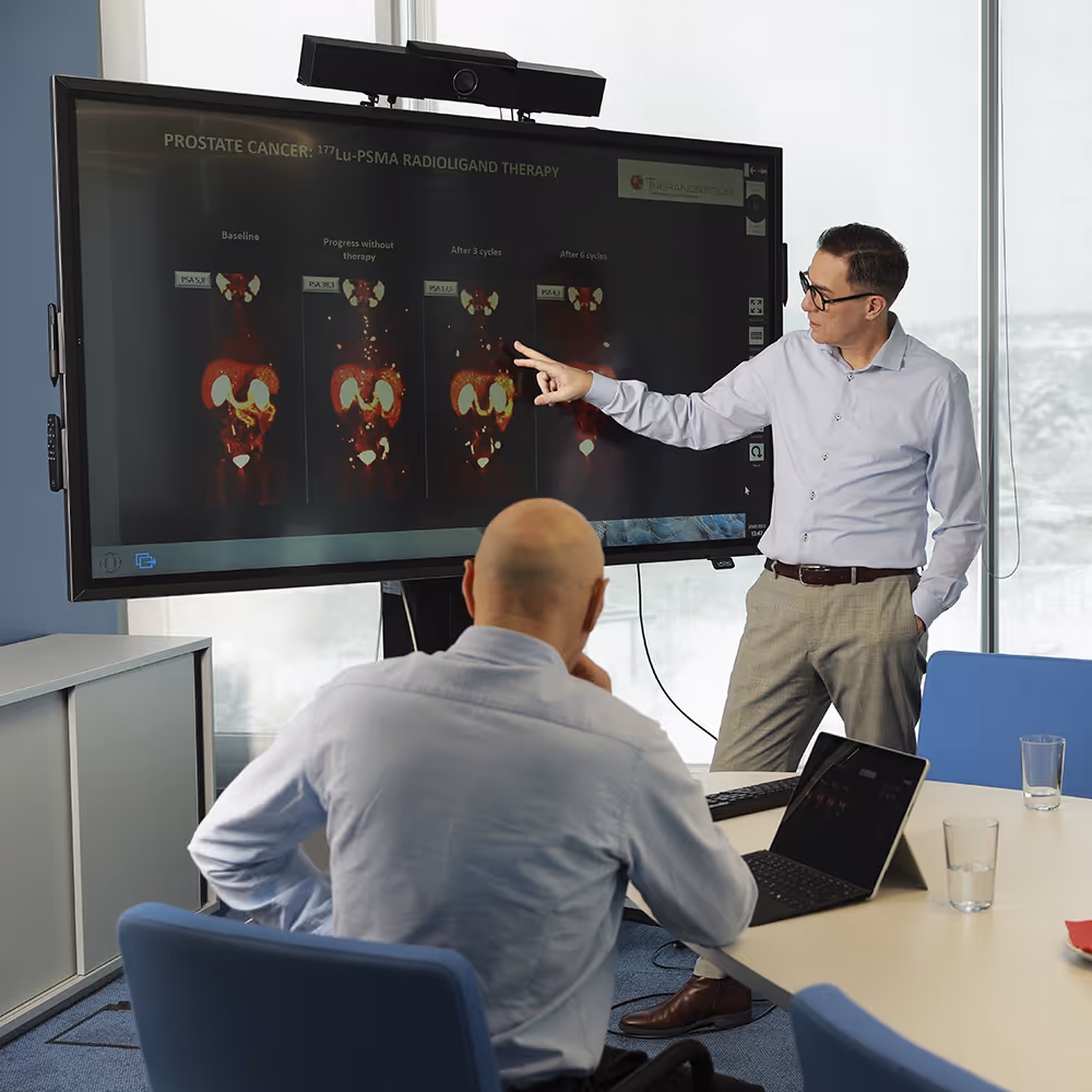 Dr. Marcus Hacker discusses medical imaging related to prostate cancer therapy with Dr. Werner Langsteger on a large screen at Theranosticum Vienna.