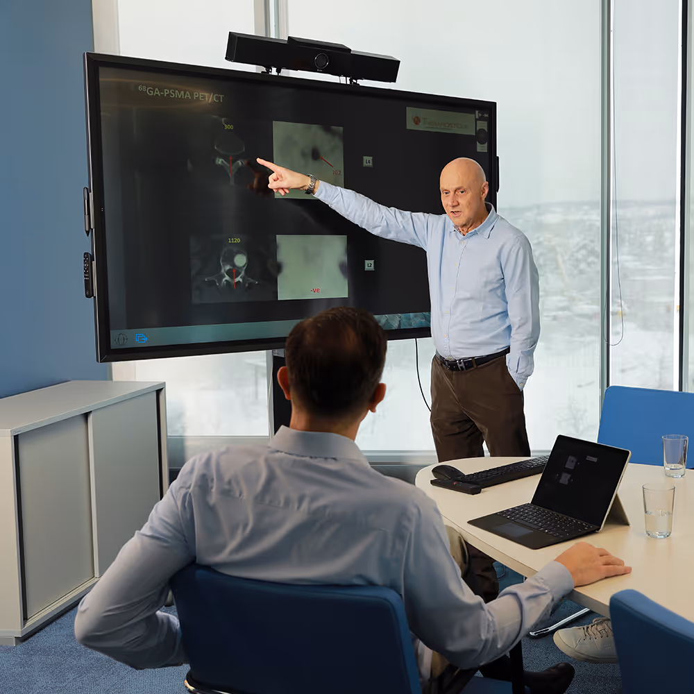 Dr. Werner Langsteger zeigt auf medizinische Bildgebung auf großem Bildschirm während einer Besprechung mit Dr. Marcus Hacker.