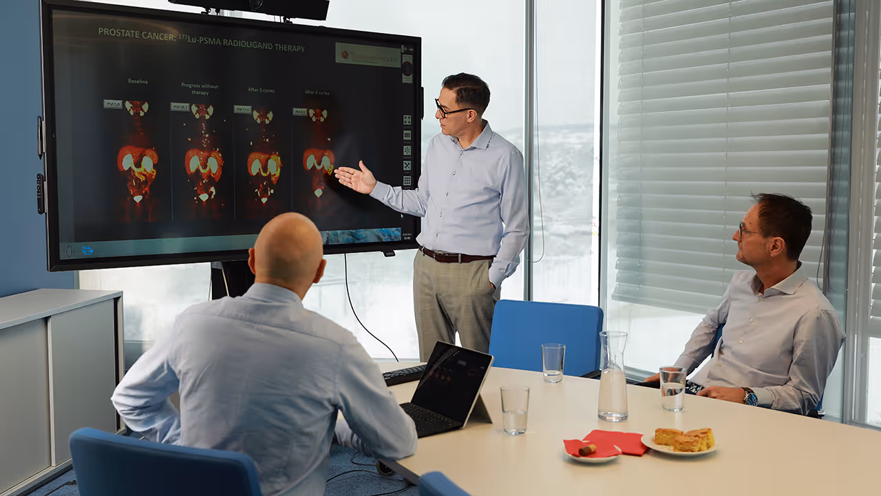 Das Ärzteteam des Theranosticum in einem Konferenzraum, Dr. Marcus Hacker erklärt Prostata-Krebs-Bilder von 177Lu-PSMA-Radioligandentherapie auf einem Bildschirm.