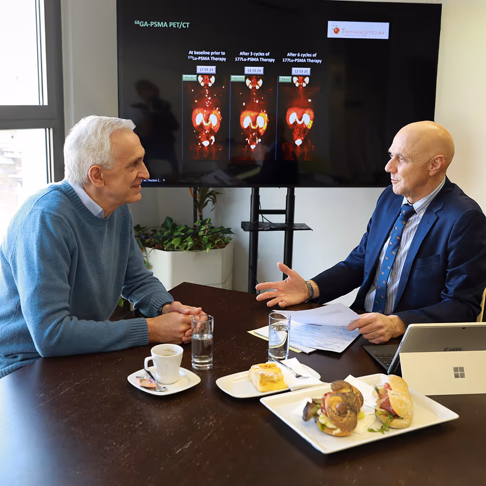 Dr. Werner Langsteger sitzt mit einem Pateinten an einem Tisch, während sie medizinische Bilder einer PSMA-PET/CT-Therapie auf einem Bildschirm besprechen.