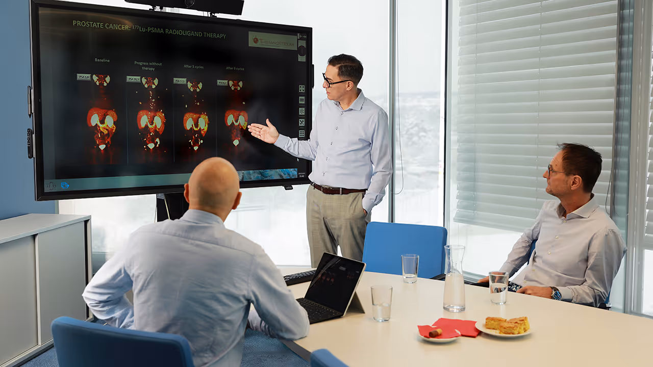 The medical team at Theranosticum in a conference room; Dr. Marcus Hacker is explaining prostate cancer images from 177Lu-PSMA radioligand therapy on a screen.