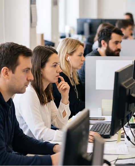 A group of focused young professionals working at computers in an office setting.