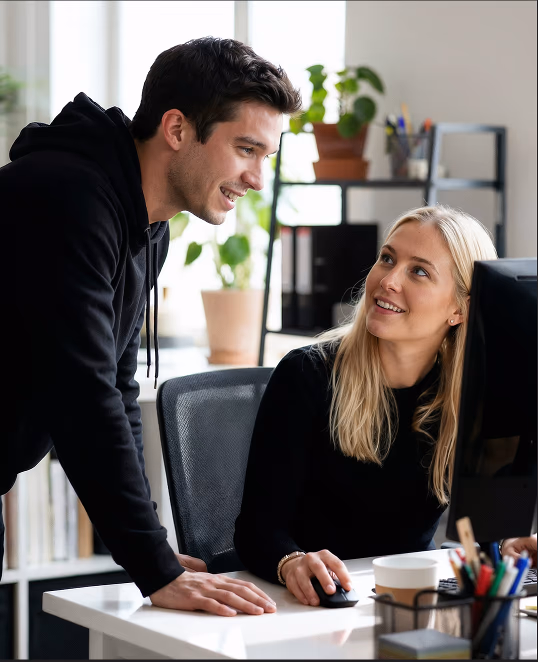 Two young adults, a woman and a man, smiling and looking at a laptop screen together.