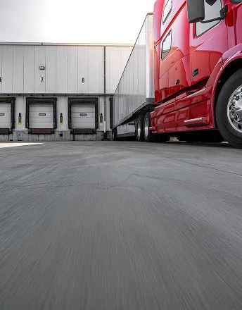 Red semi-truck backed into a loading dock at a warehouse with numbered dock doors.