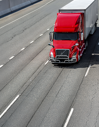 Red semi-truck with a white trailer driving on a multi-lane highway.