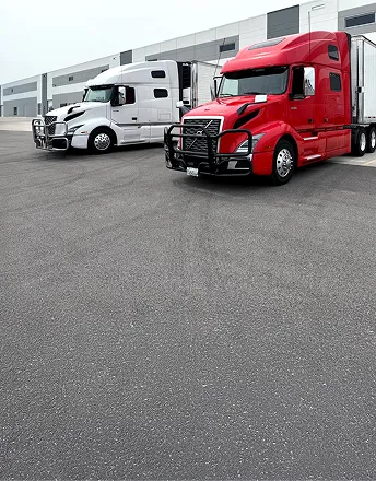Red and white semi-trailer trucks parked side by side in front of a warehouse.