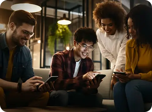 Four young adults sitting indoors looking at smartphones and smiling in a cozy setting.