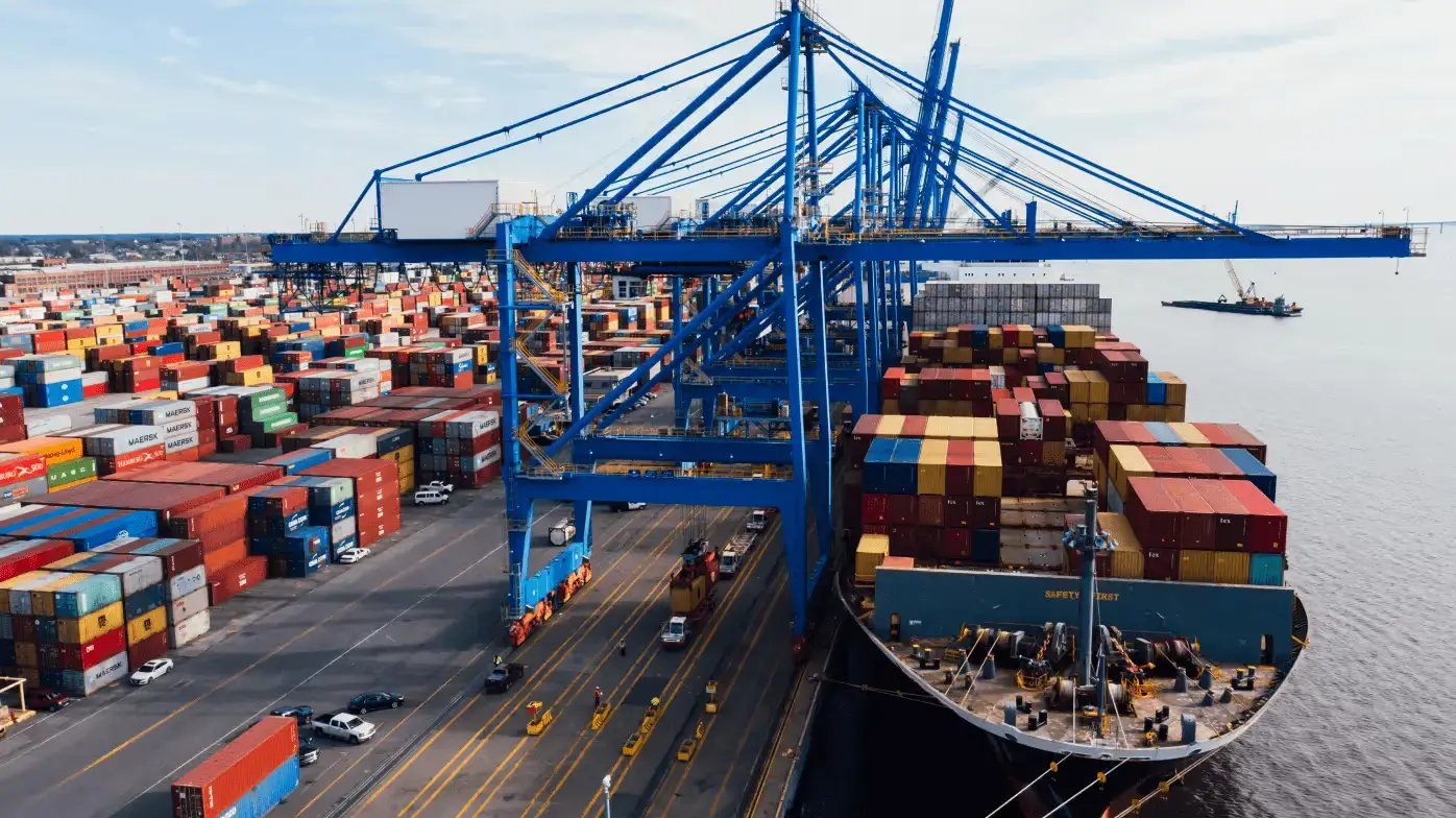 Large cargo ship docked at port with cranes unloading colorful shipping containers.