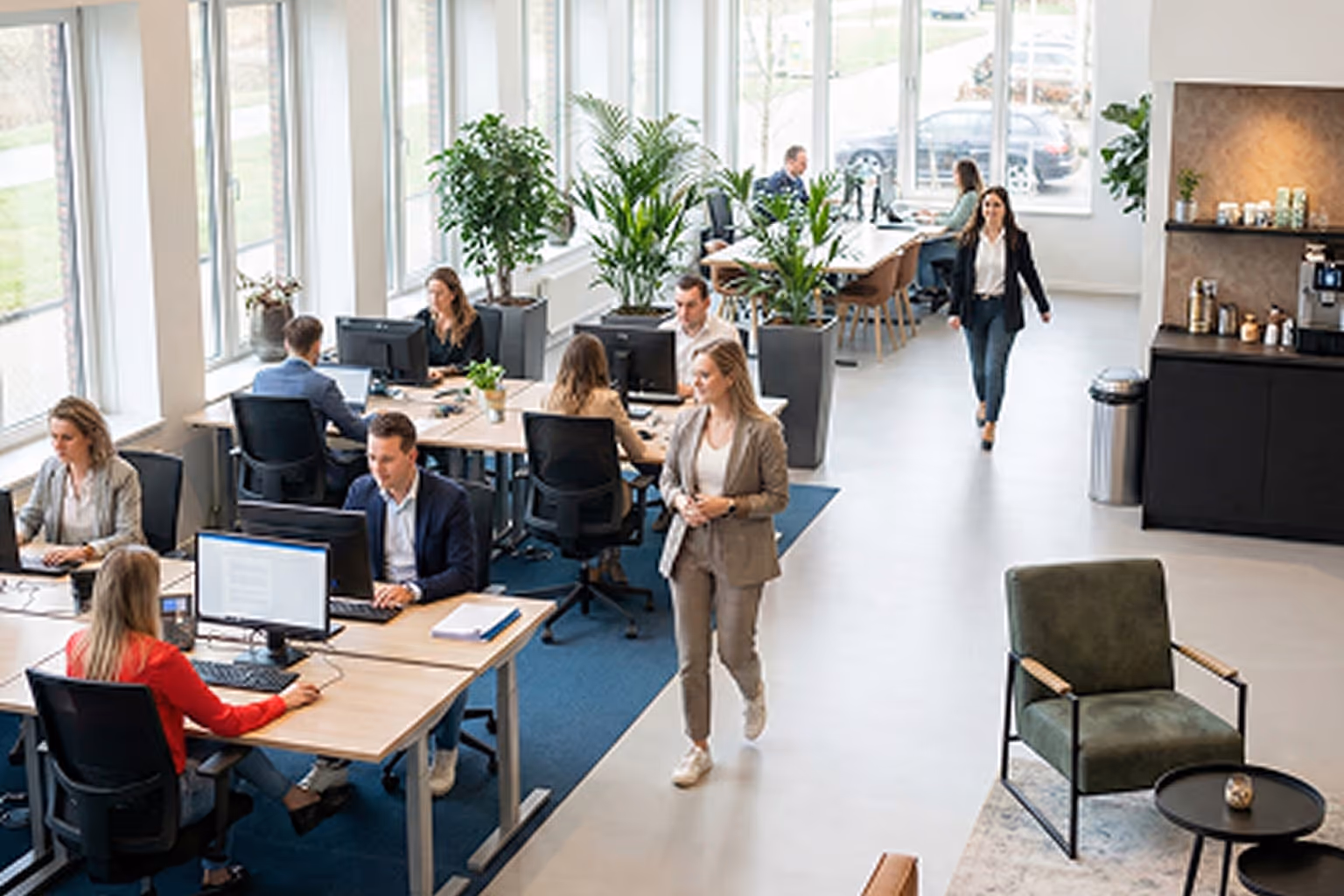 Moderne kantoorruimte met recruiters die aan bureaus werken en twee vrouwen lopen langs het gangpad.