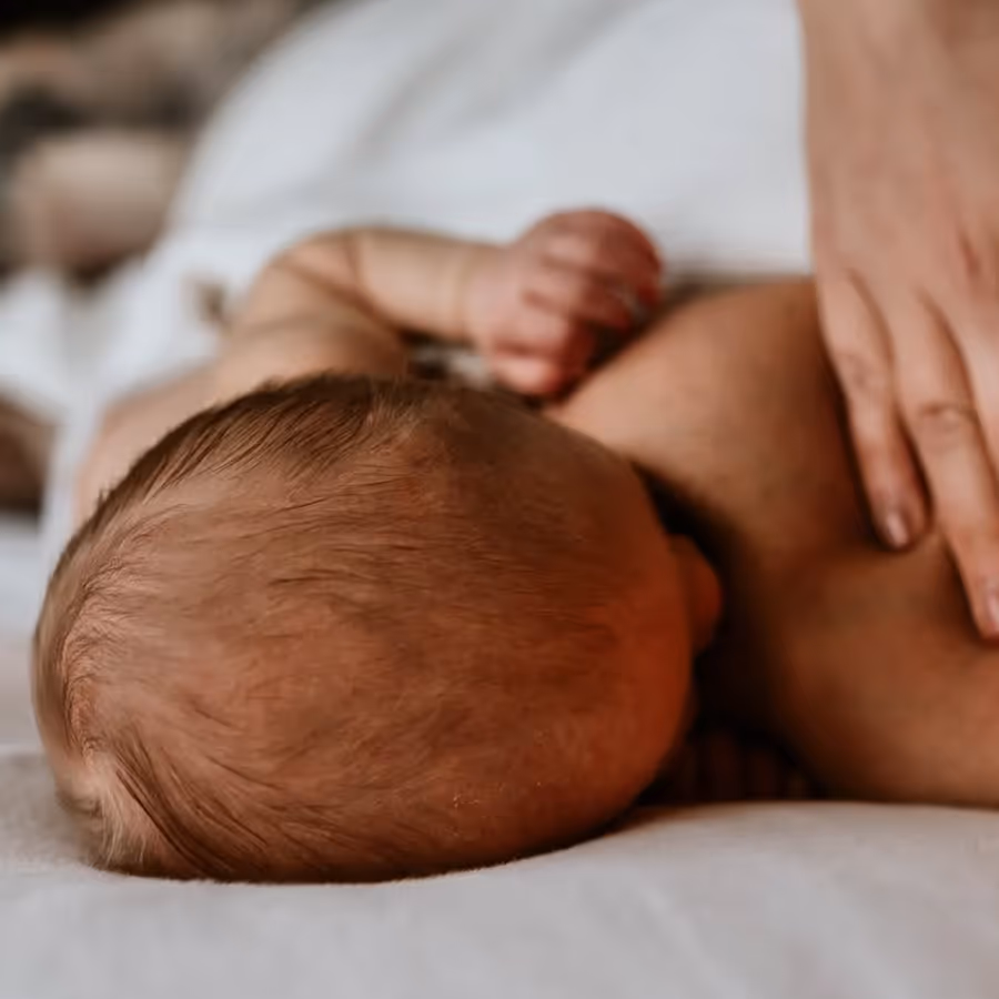 Een baby die wordt borstvoed door een volwassene met een hand op de baby's schouder.