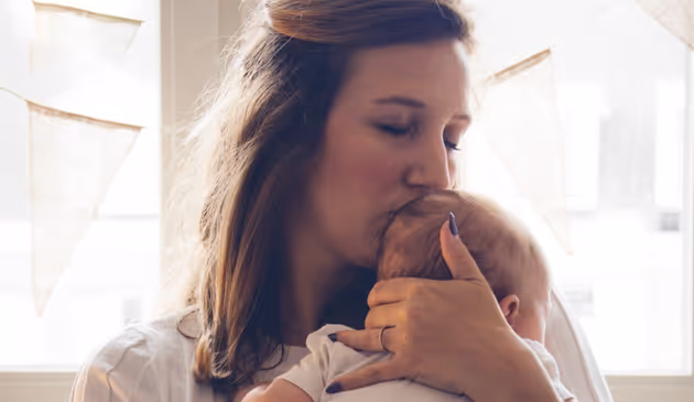 Vrouw kust liefdevol de schedel van een baby terwijl ze het stevig vasthoudt.