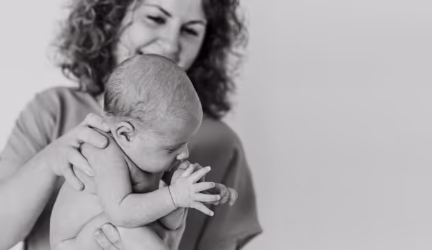 Vrouw die een baby vasthoudt met een glimlach, in zwart-wit foto.
