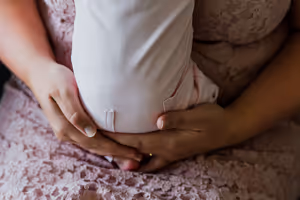 Twee handen die voorzichtig een baby omsluiten die op een roze kanten jurk ligt.