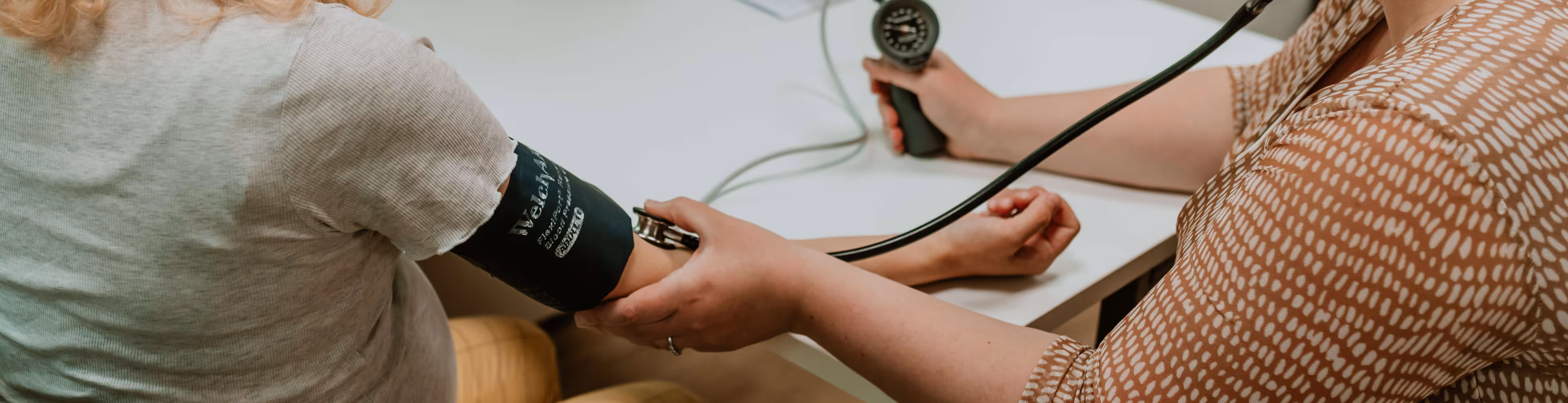 Een zorgverlener neemt de bloeddruk op bij een patiënt met behulp van een bloeddrukmanchet en een stethoscoop.
