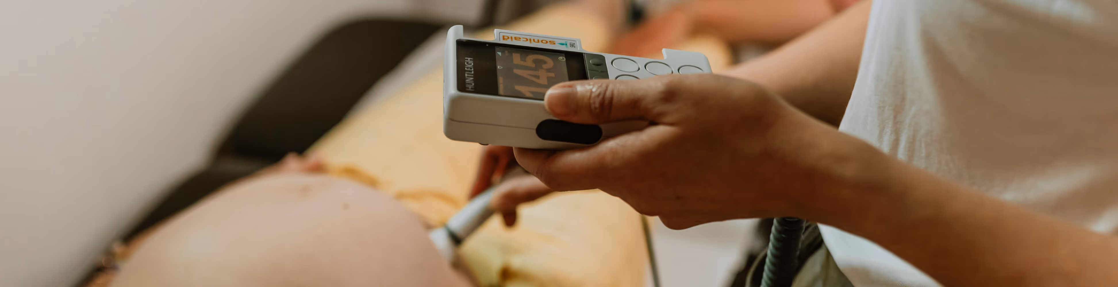 Een hand die een medisch apparaat vasthoudt voor het meten van vitale functies bij een zwangere vrouw.