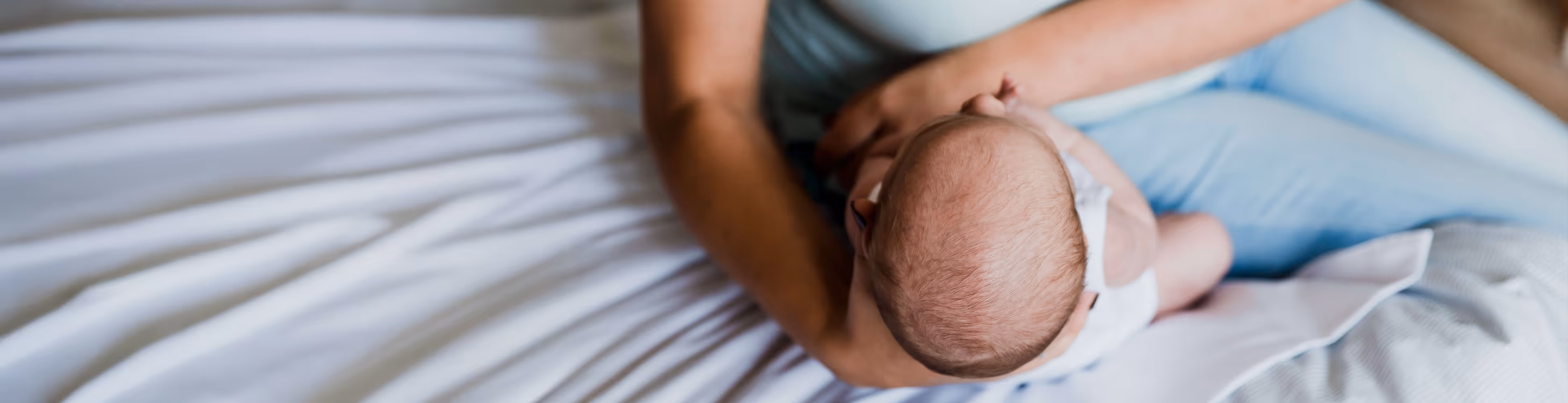 Een moeder die haar baby in haar armen houdt terwijl ze op een bed zit.