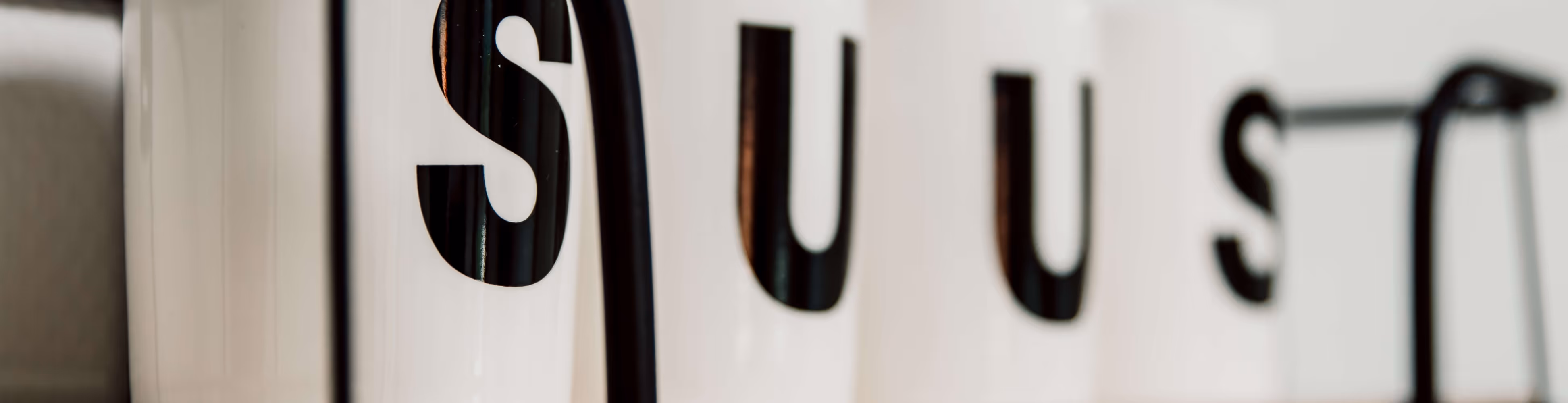 Witte mokken met zwarte letters die samen het woord SUUS vormen op een rij.