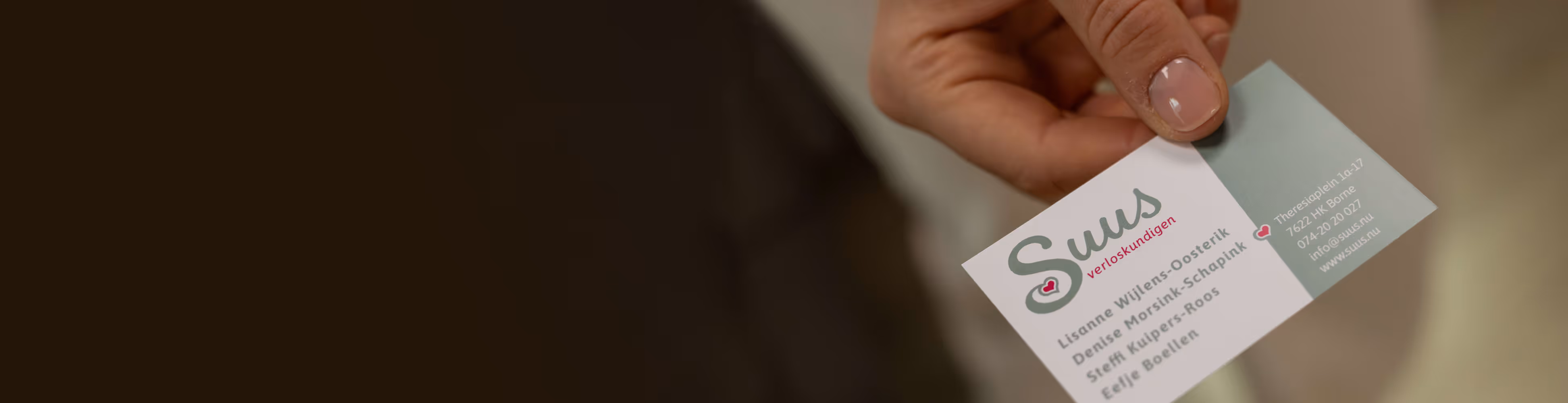 Hand houdt visitekaartje van Suus verloskundigen met namen en contactgegevens.