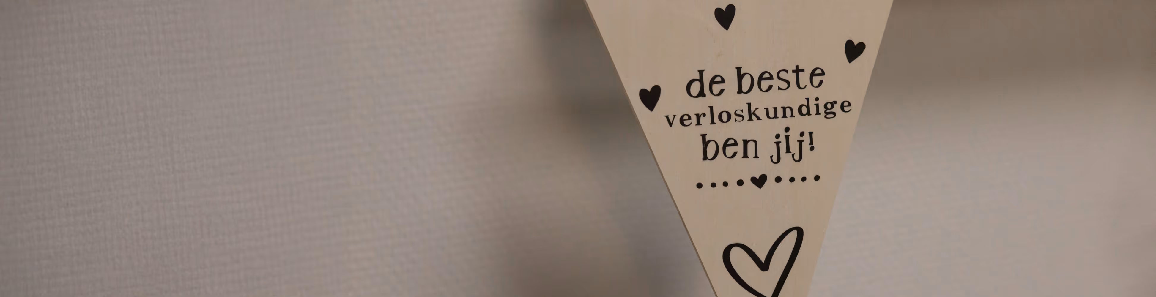 Een houten driehoek met de tekst 'de beste verloskundige ben jij!' en omlijst met kleine hartjes.