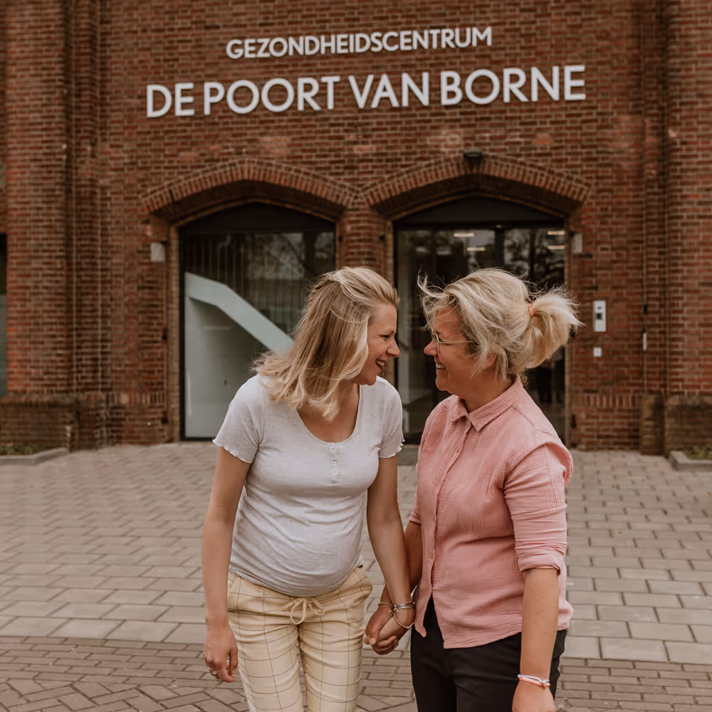 Twee vrouwen die elkaar vasthouden en lachen voor Gezondheidscentrum De Poort van Borne.