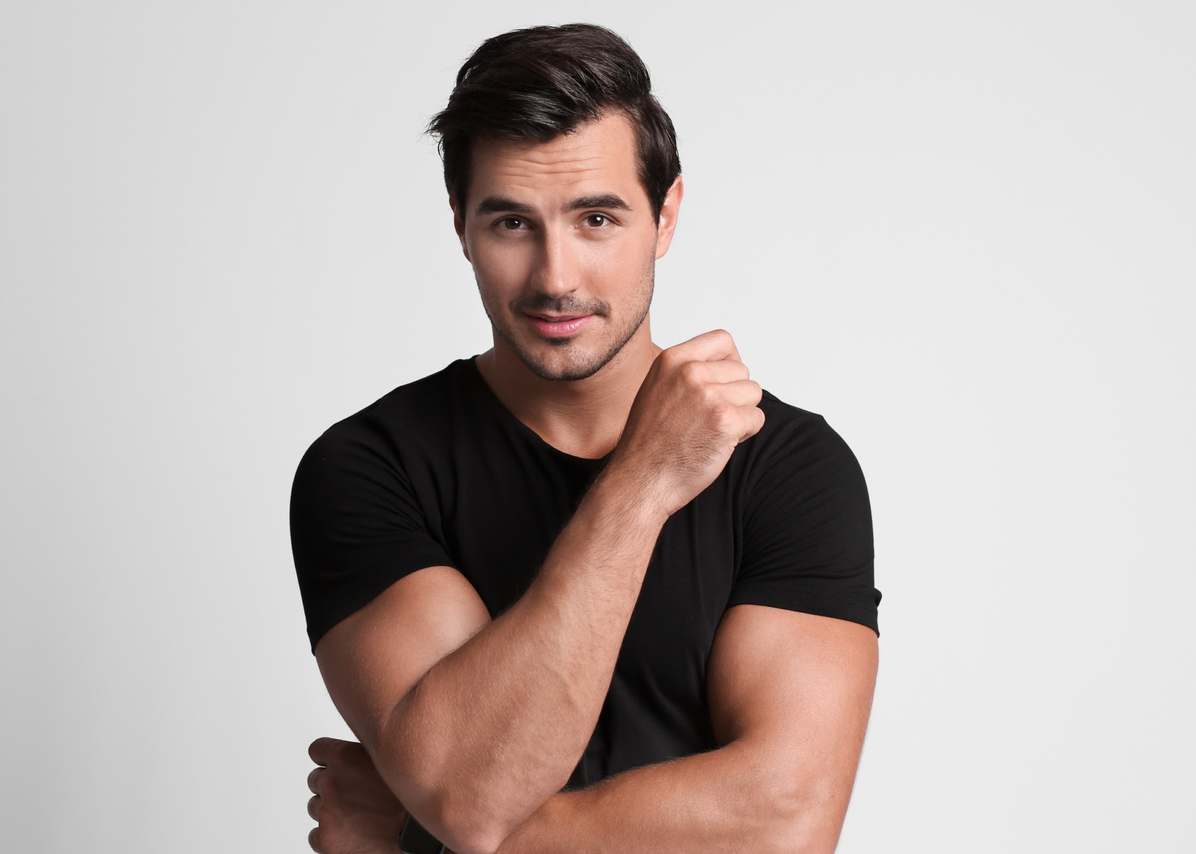 Confident man with dark hair wearing a black t-shirt, crossing his arms and looking at the camera.
