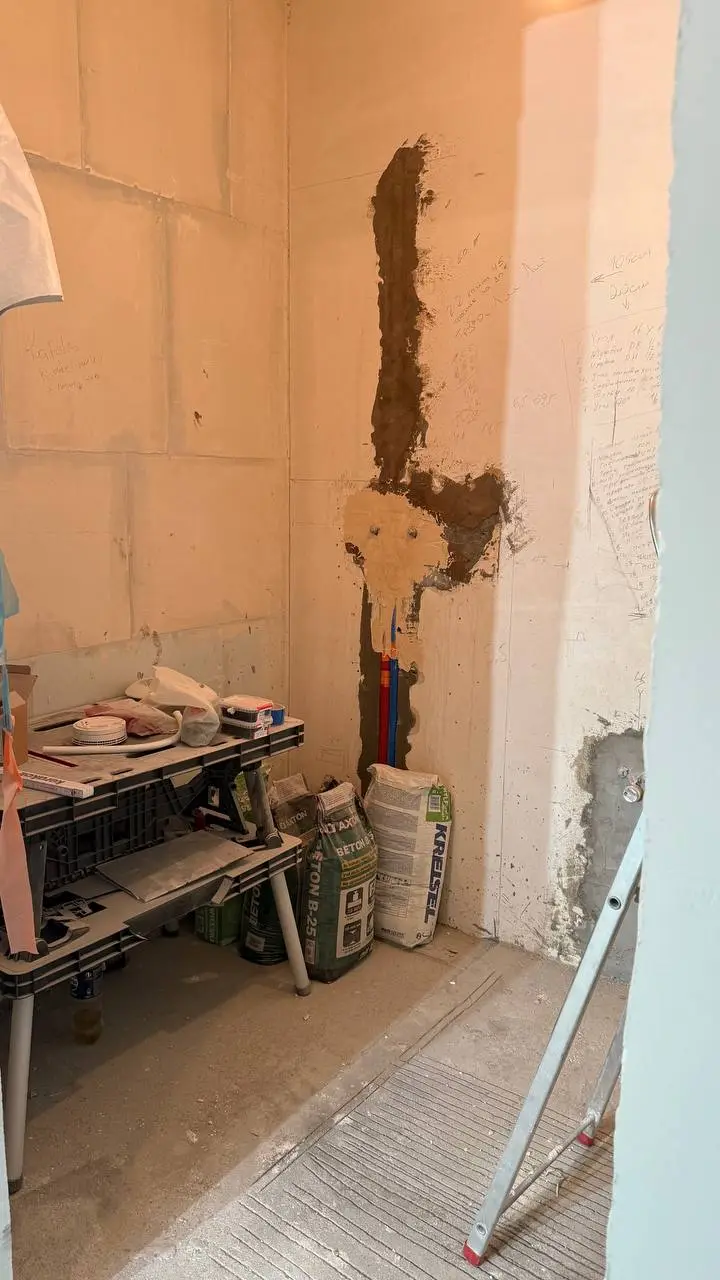 Pomieszczenie w budowie z regałem na narzędzia, workami z materiałami budowlanymi i drabiną.