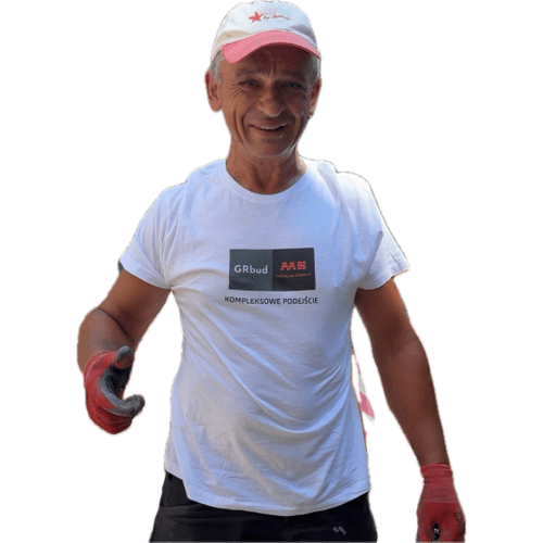 Uśmiechnięty mężczyzna w białej koszulce z logo GRbud i ABB oraz napisem Kompleksowe podejście, w czerwonych rękawicach i białej czapce z czerwonym daszkiem.
