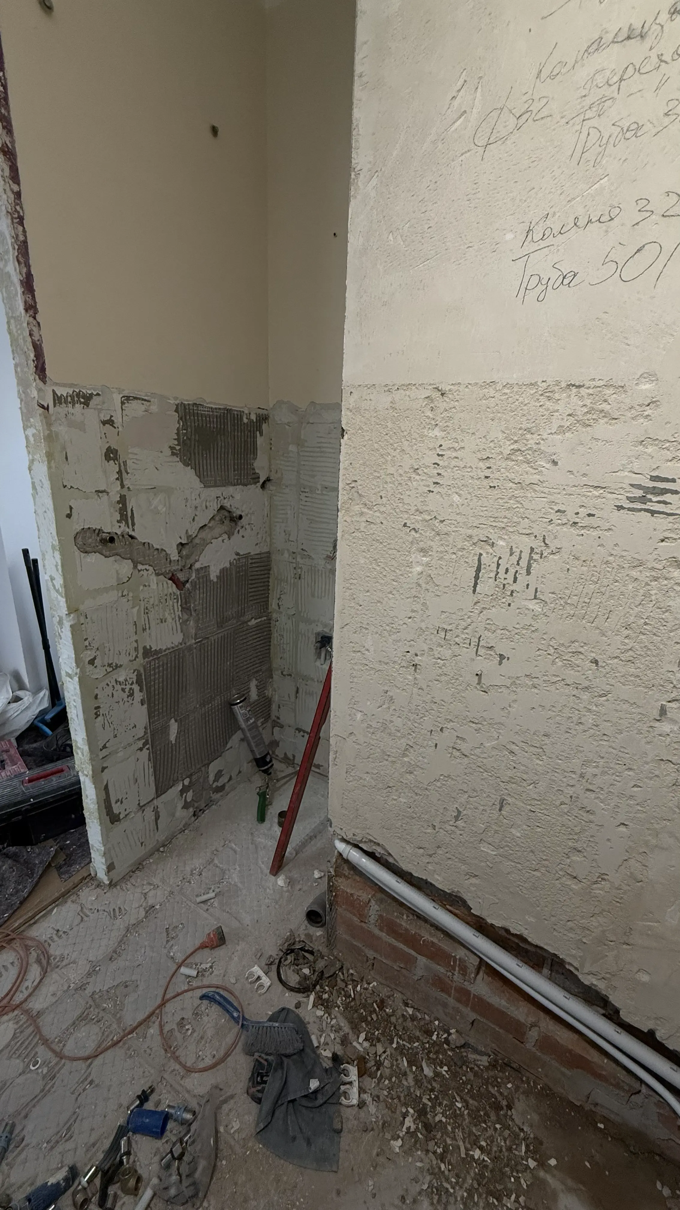 Pomieszczenie w trakcie remontu z odsłoniętymi ścianami, rurami i narzędziami budowlanymi na podłodze.