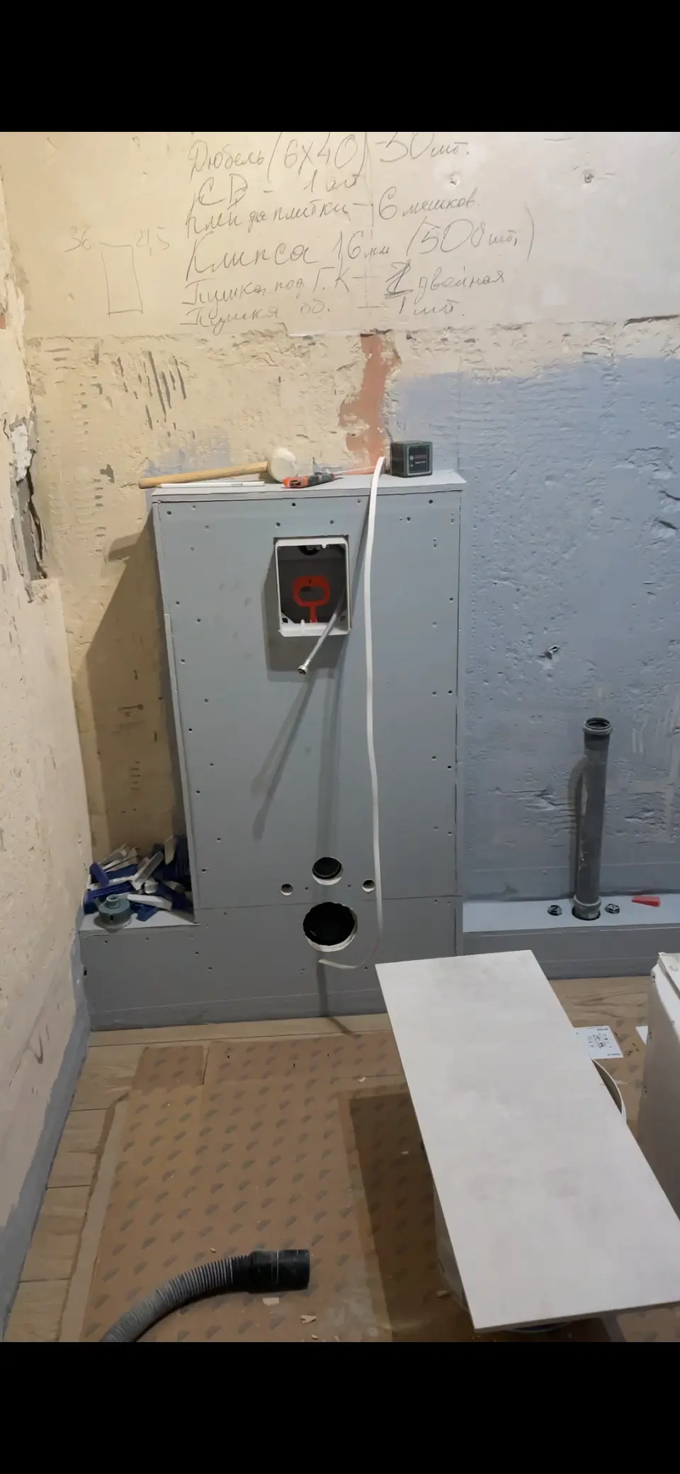 Niedokończone prace instalacyjne w łazience z zamontowanym szarym stelażem podtynkowym do WC i widocznymi rurami oraz narzędziami.