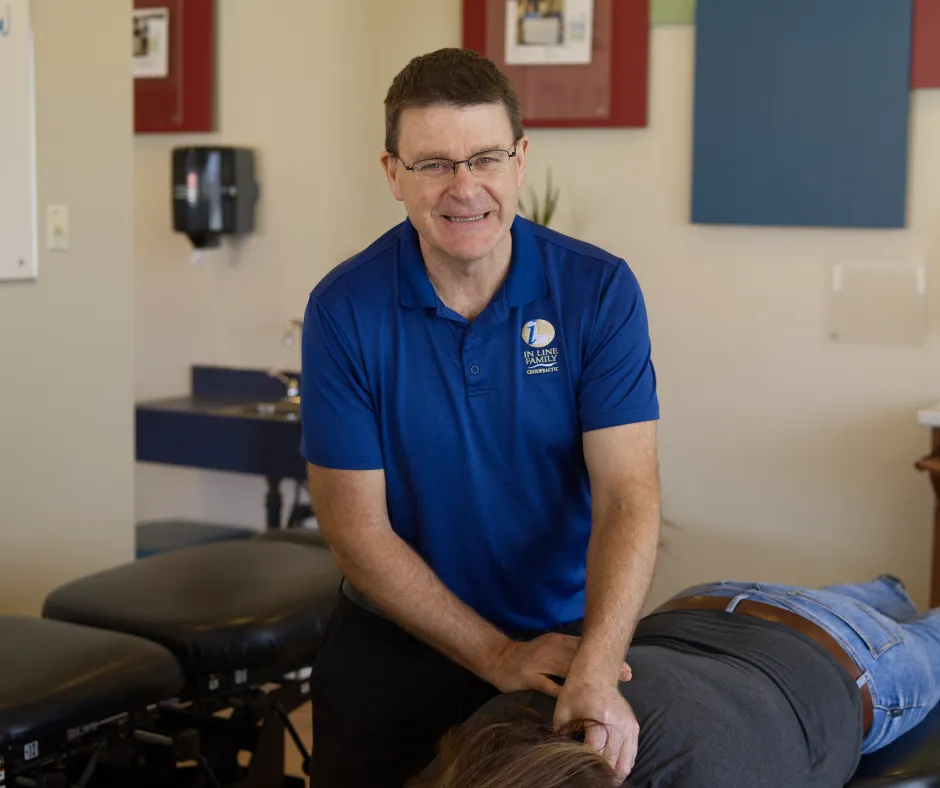 Chiropractor in a blue shirt with 'In Line Family Chiropractic' logo performing a spinal adjustment on a patient lying face down.