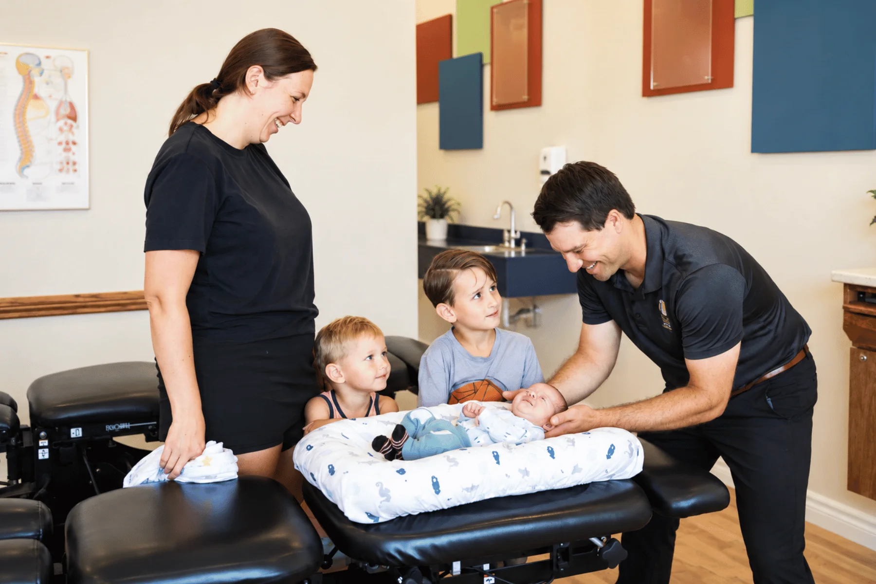 Dr. Adam Alexander gently adjusting a newborn as the baby’s mum and two young brothers stand next to them