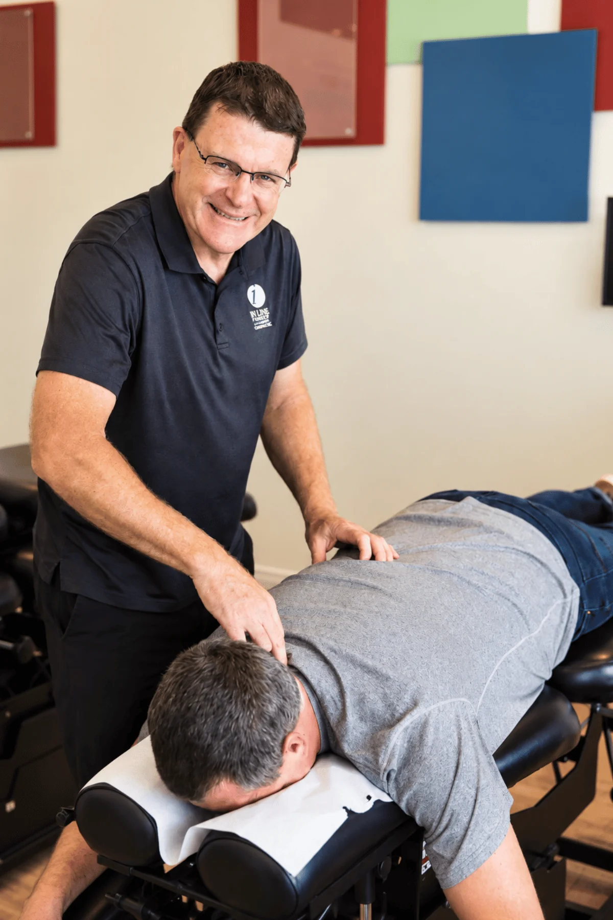 Dr. Glenn Lang smiling as he adjusts the upper back of a patient lying face down on a chiropractic table