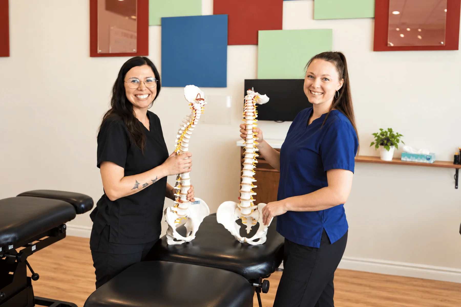 Two smiling In Line Family Chiropractic team members holding spine models in the clinic