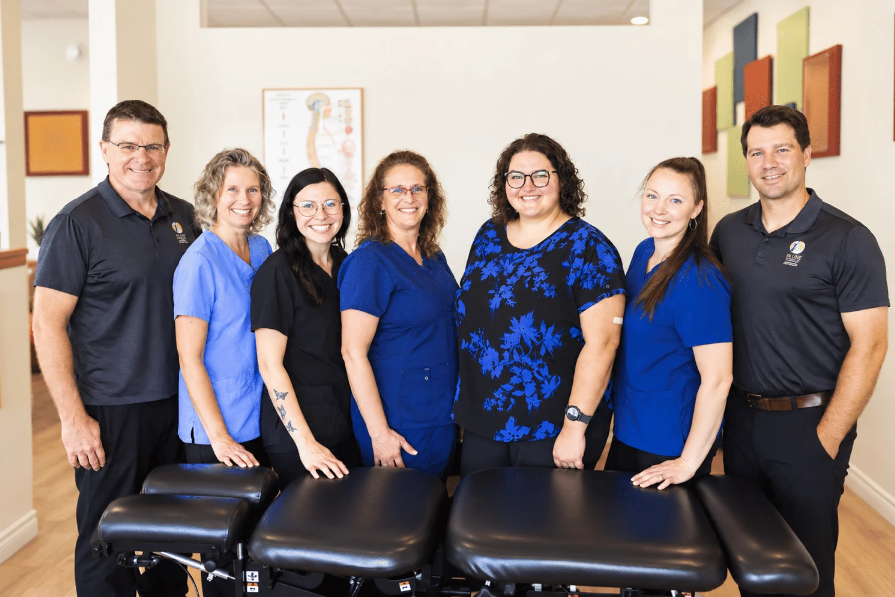 The In Line Family Chiropractic team of seven standing behind adjusting tables in the clinic