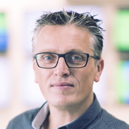 Middle-aged man with spiked gray hair and black glasses wearing a dark collared shirt.