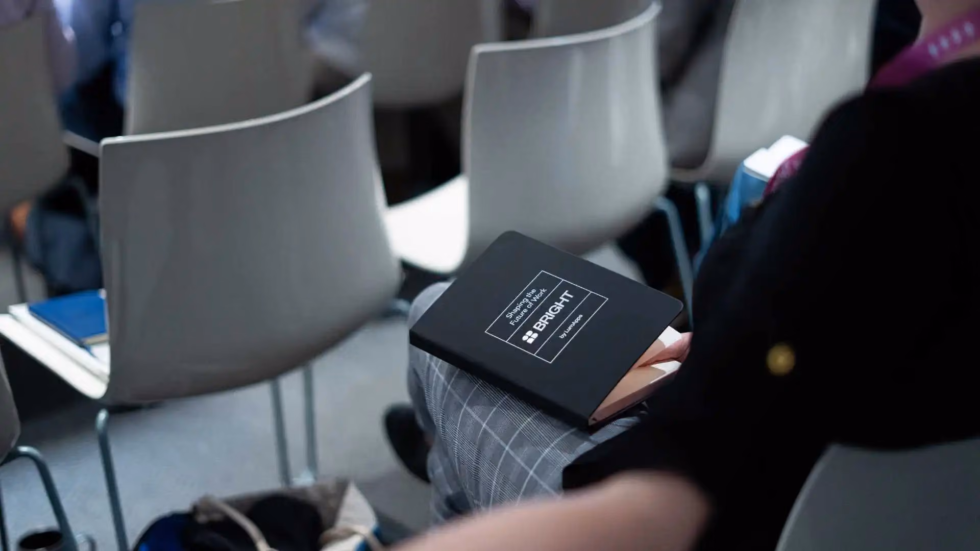 Person seated holding a black notebook displaying text 'Shaping the Future of Work BRIGHT'.