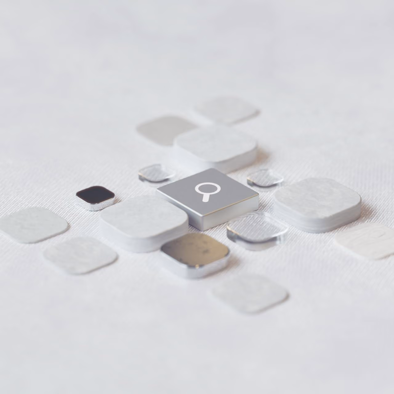 Silver key with a magnifying glass icon among white and transparent square blocks on a white surface.