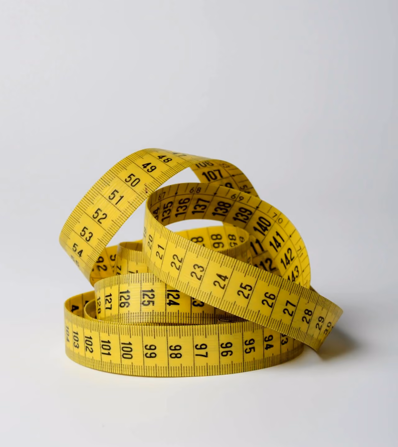 Coiled yellow tape measure with black numbers on a white surface.