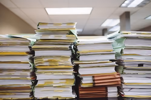 Stacks of thick documents with multiple sticky notes on each, organized on a desk in an office.