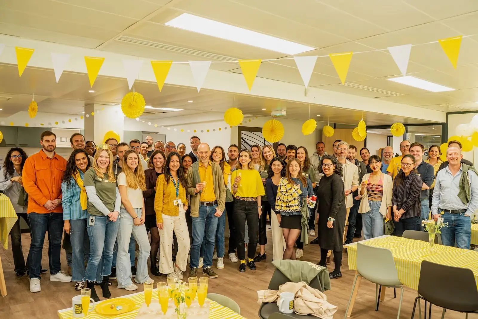 Large group of people smiling at a yellow and white decorated indoor party event.